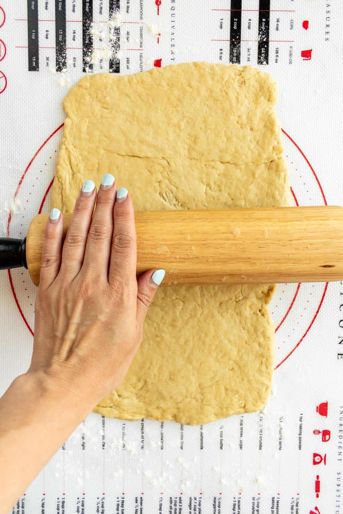 A hand rolling out cinnamon roll dough with a wooden rolling pin.