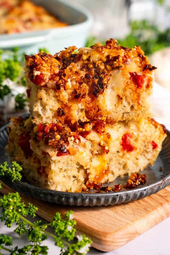 Two large squares of pizza focaccia stacked on a plate next to sprigs of oregano.