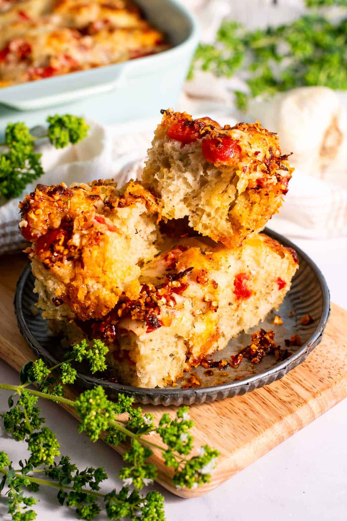 Stacked pieces of focaccia bread topped with tomatoes, melted cheese, and chili oil crisp on a metal plate.