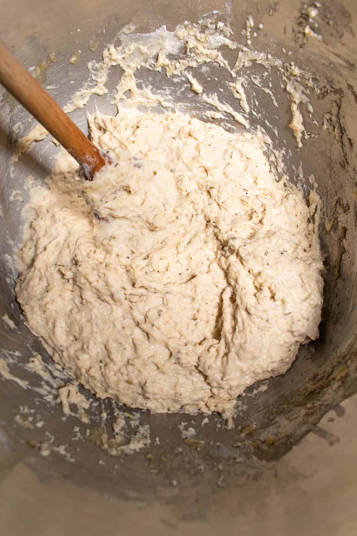 Wet, sticky focaccia dough in a metal bowl with a large wooden spoon.