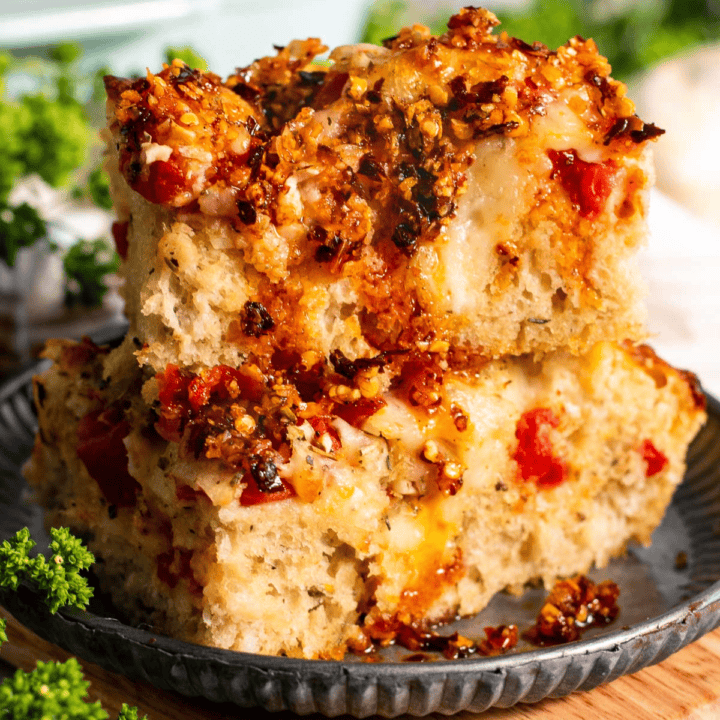 Two large squares of focaccia topped with garlic, tomatoes, and cheese stacked on a plate.