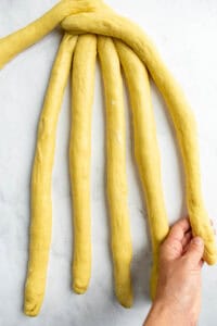 A hand braiding challah bread on a light surface.