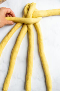 A hand braiding challah bread on a marble counter.