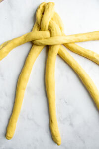 A partially braided loaf of challah on a marble counter.