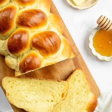 A loaf of braided challah bread on a cutting board next to a few slices.