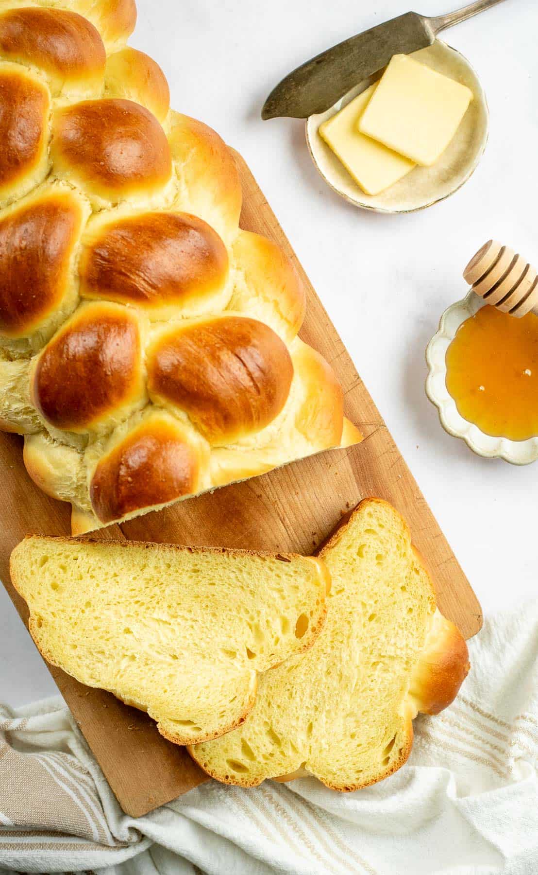 A loaf of braided challah bread on a cutting board next to a few slices. 