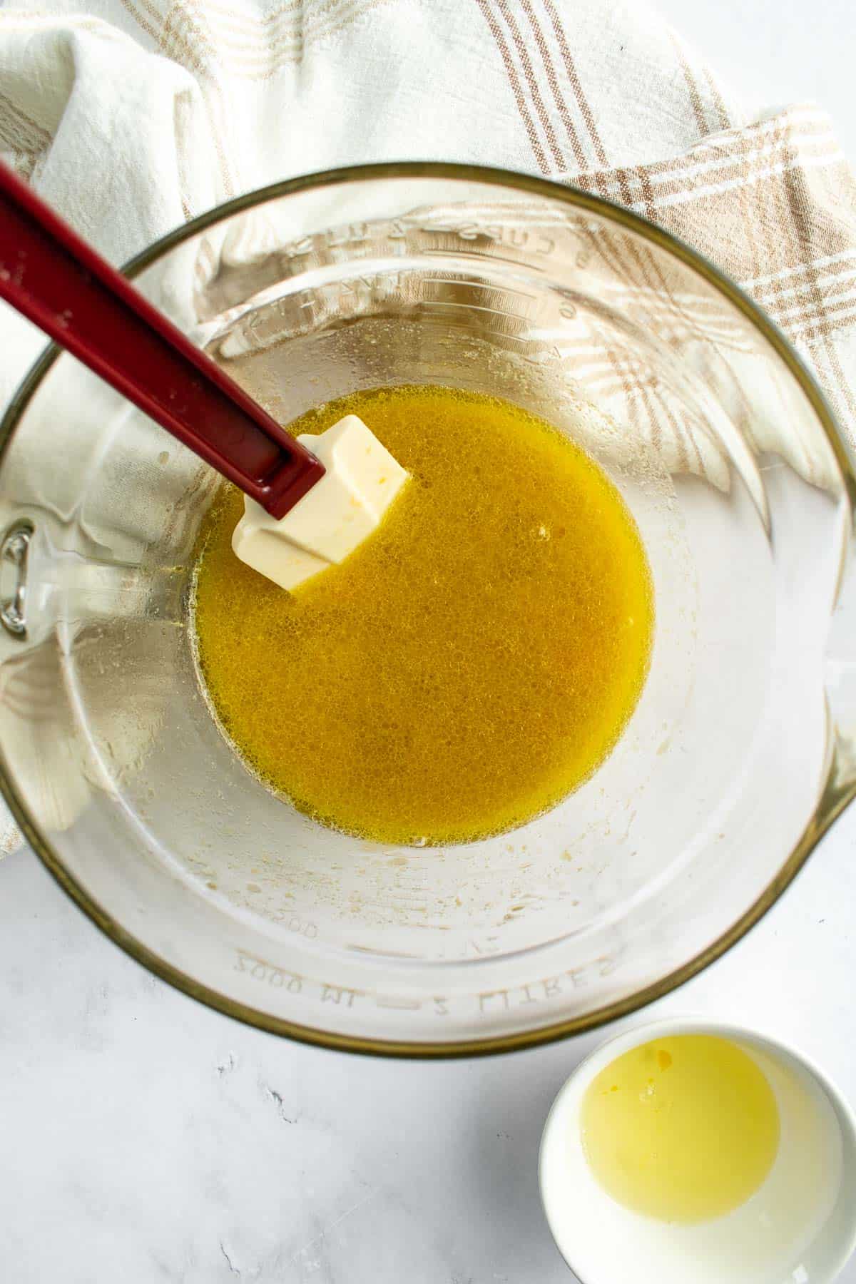 Olive oil, yeast, sugar, and water mixed together to form a dark yellow liquid in a glass mixing bowl.