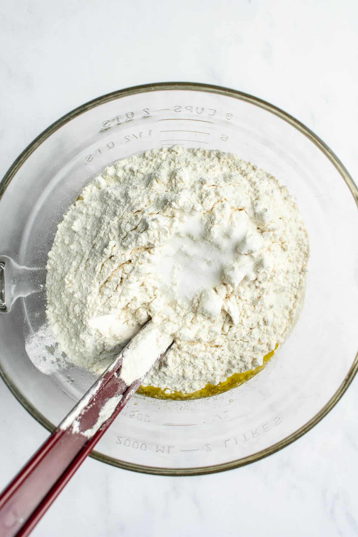 Flour and salt sifted into a glass mixing bowl on a light surface.