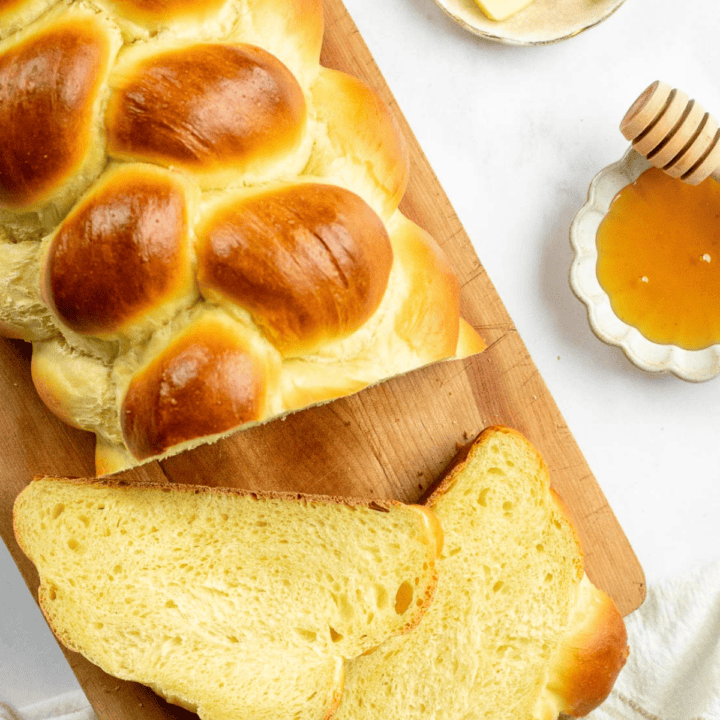 A loaf of braided bread on a wood board next to two slices of fluffy, enriched challah.