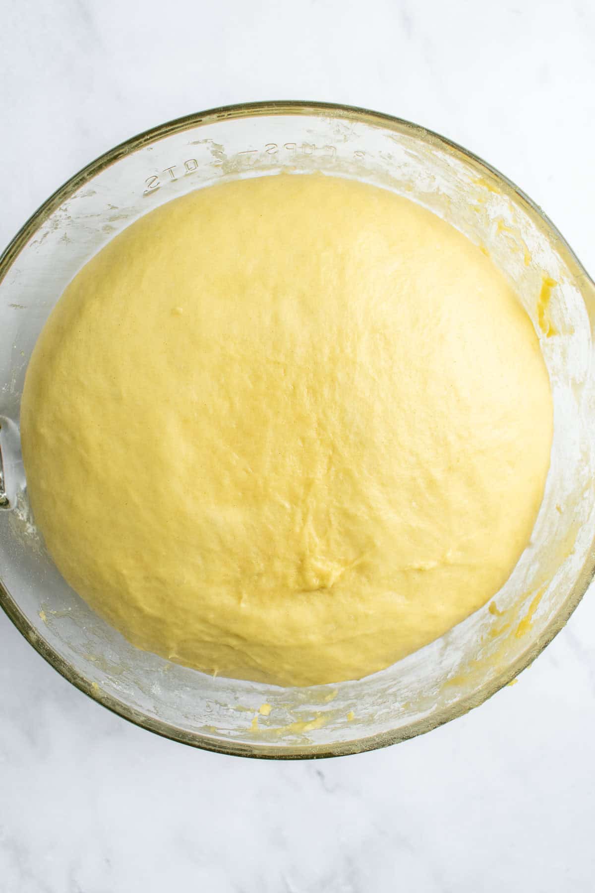 Risen, airy bread dough filling almost an entire glass mixing bowl on a light surface.