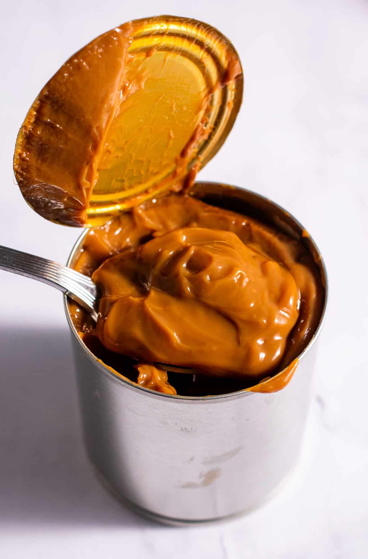A metal can filled with thick, gooey caramel sauce on a light surface.