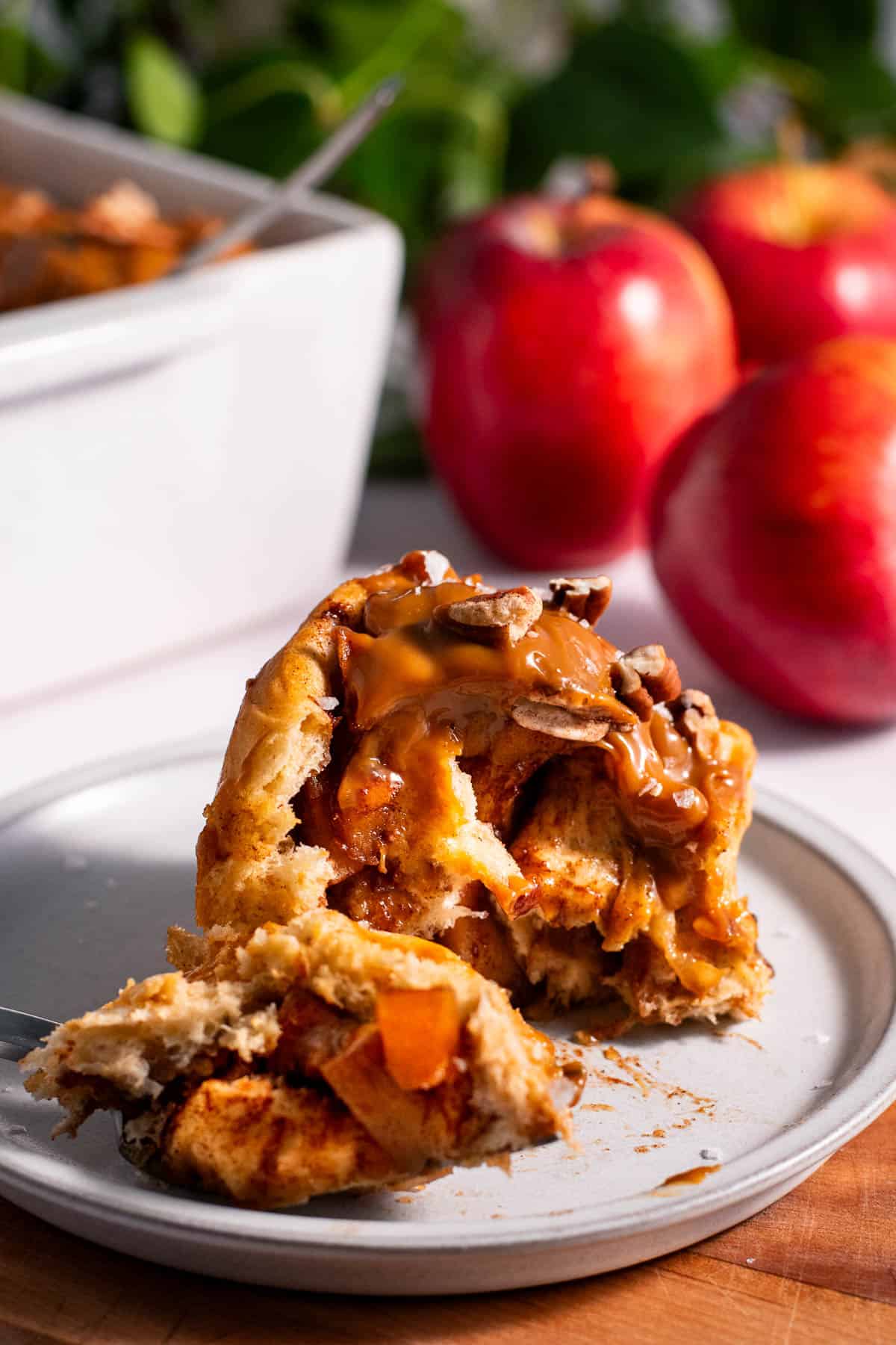 A half-eaten apple cinnamon roll on a grey plate, with small caramelized apple pieces inside.