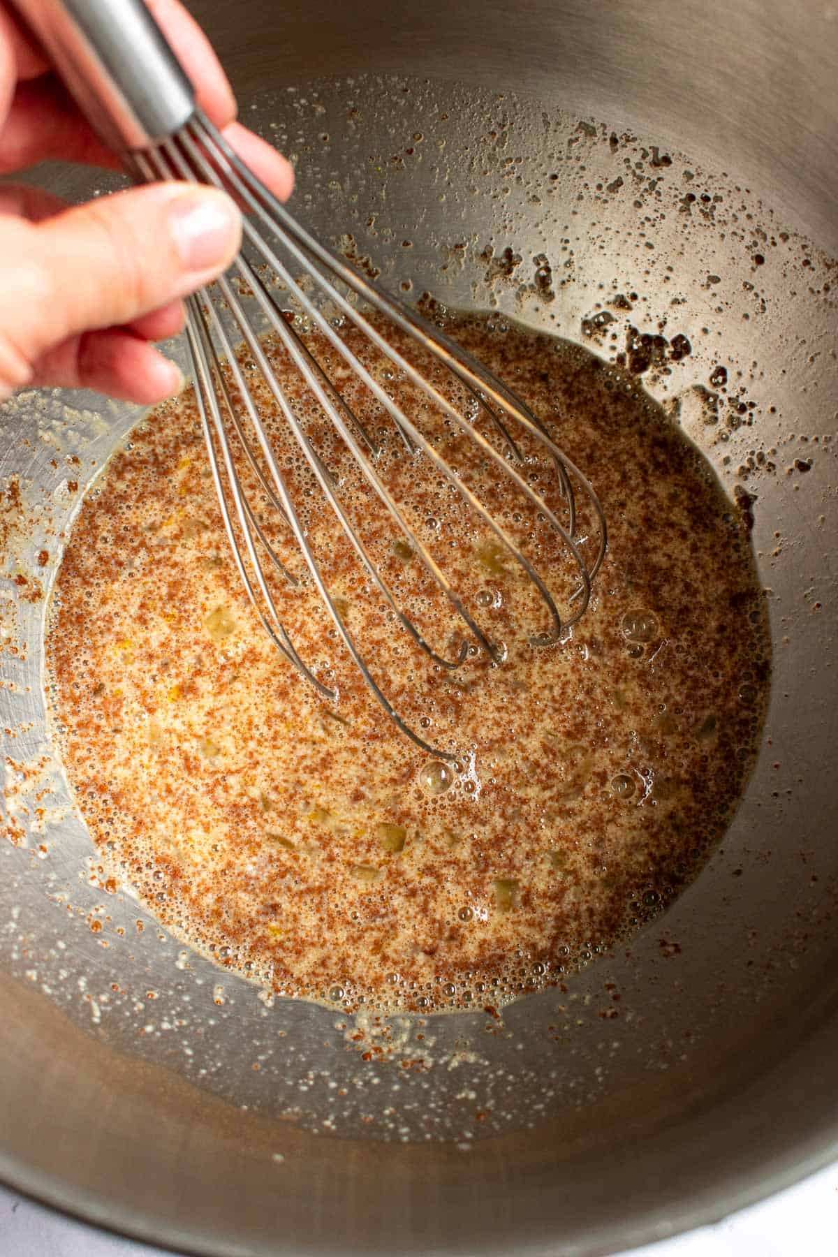 A hand whisking spices, eggs, milk, yeast, and sugar in a large metal bowl.