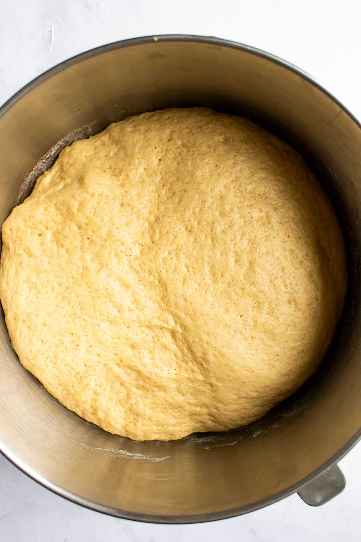 Risen bread dough in a large metal bowl on a light surface.