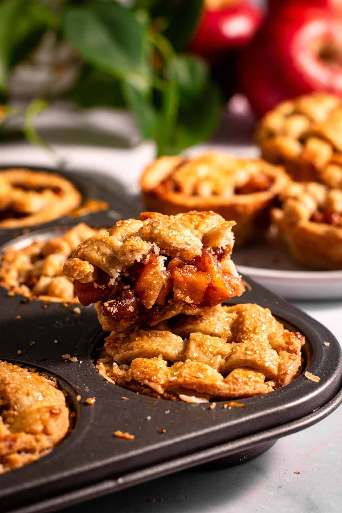 A muffin tin filled with mini pies, with a half-eaten mini apple pie sitting on top. 