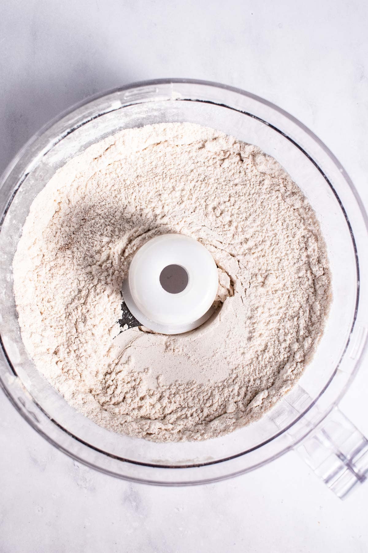 Flour sitting in a food processor on a light surface.