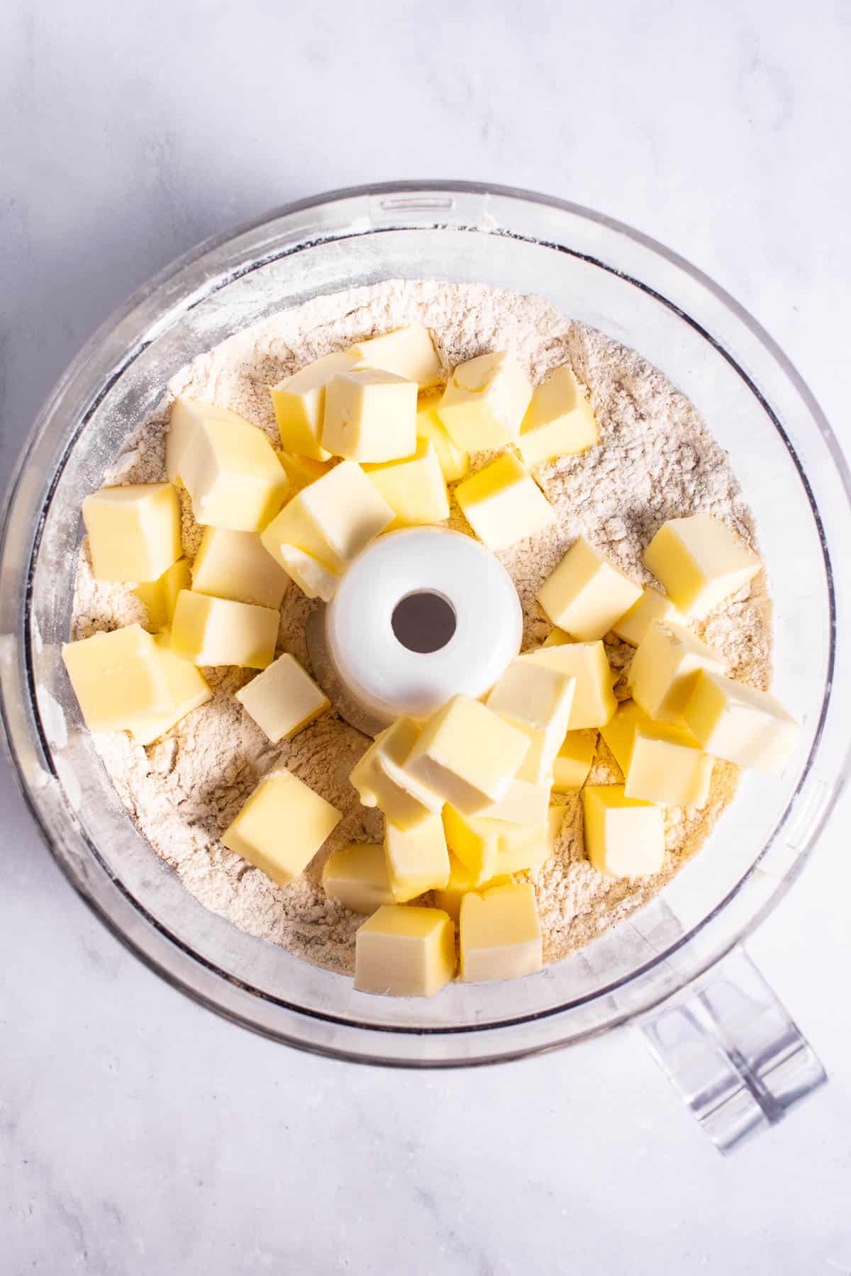 Butter cubes sitting on top of flour in a food processor.