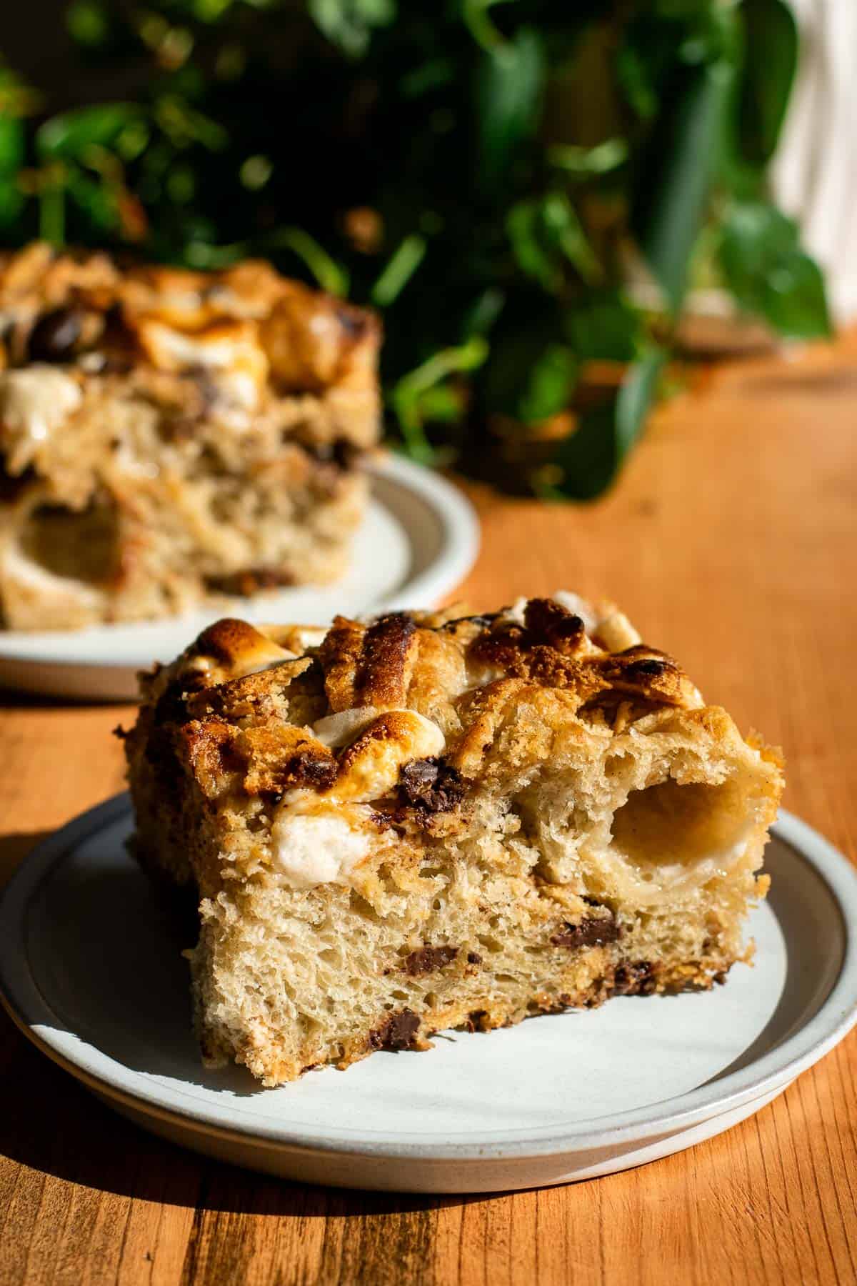 Two large pieces of focaccia on plates topped with melted chocolate, marshmallows, and crushed graham crackers.