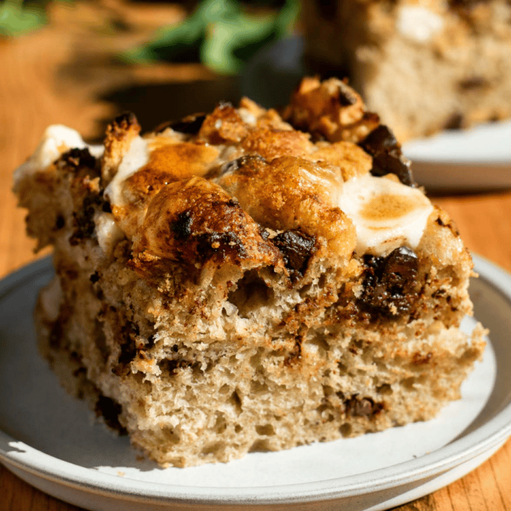 A large square of s'mores focaccia topped with marshmallows, chocolate, and graham crackers on a grey plate.