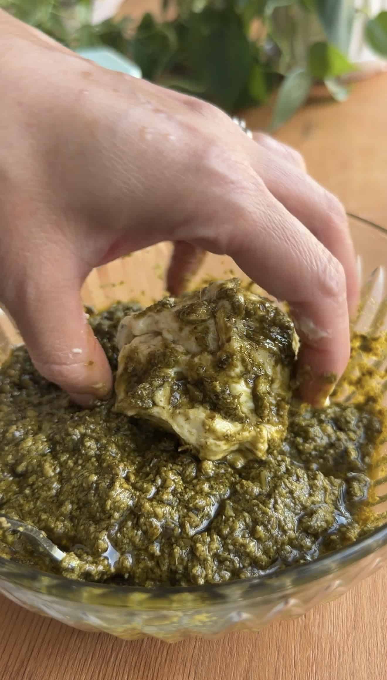 A hand rolling a ball of bread dough in a bowl of basil pesto.
