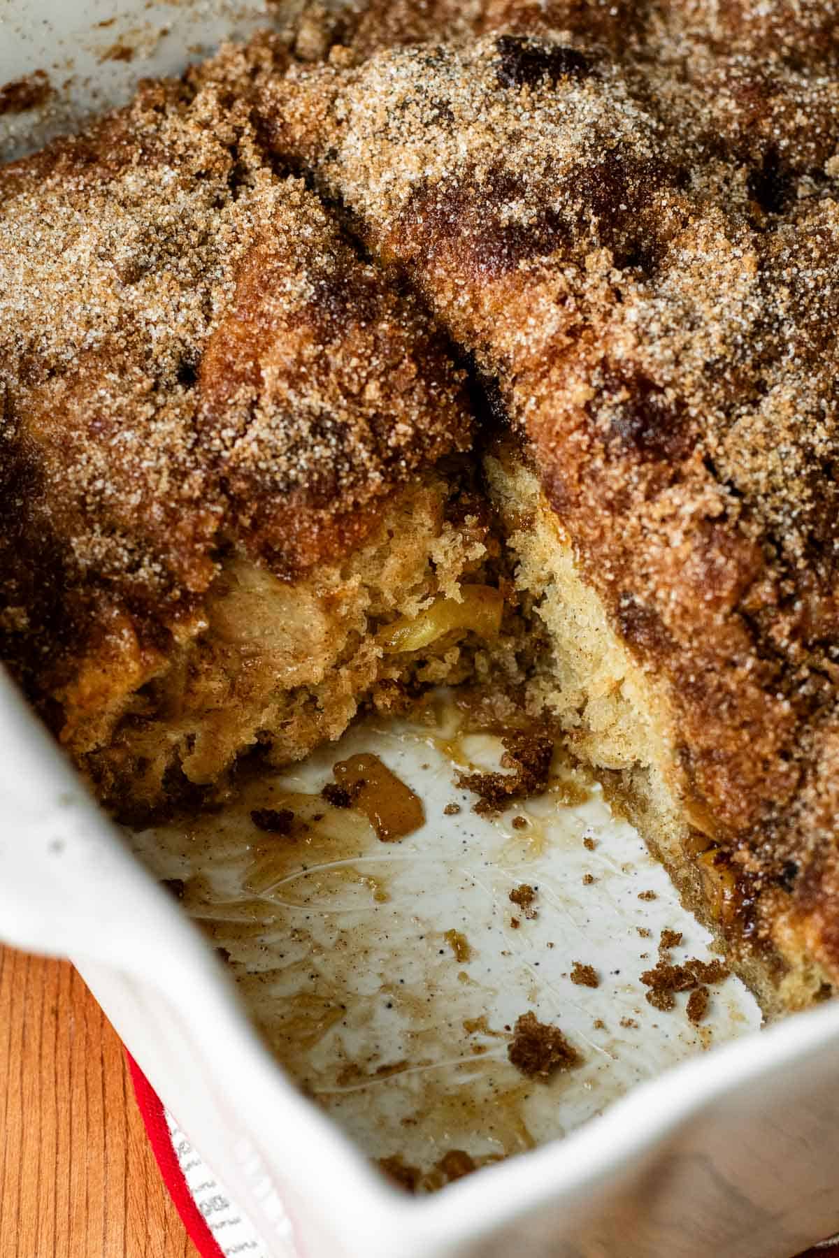 A white casserole dish filled with sugar-crusted apple focaccia, with one large square missing from the dish.