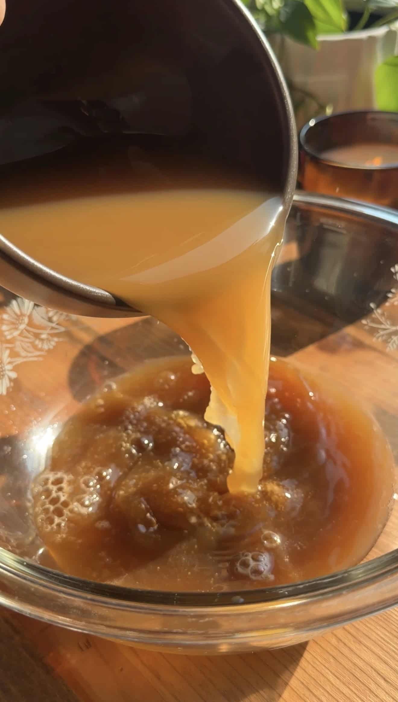 Apple juice being poured from a brown bowl into a mixing bowl with sugar and yeast.