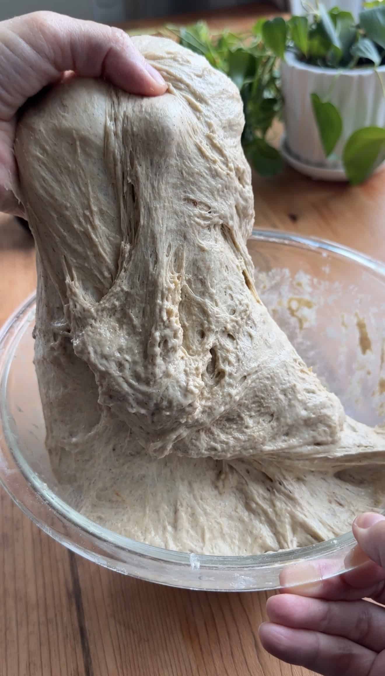 A hand pulling dough up out of a glass mixing bowl.
