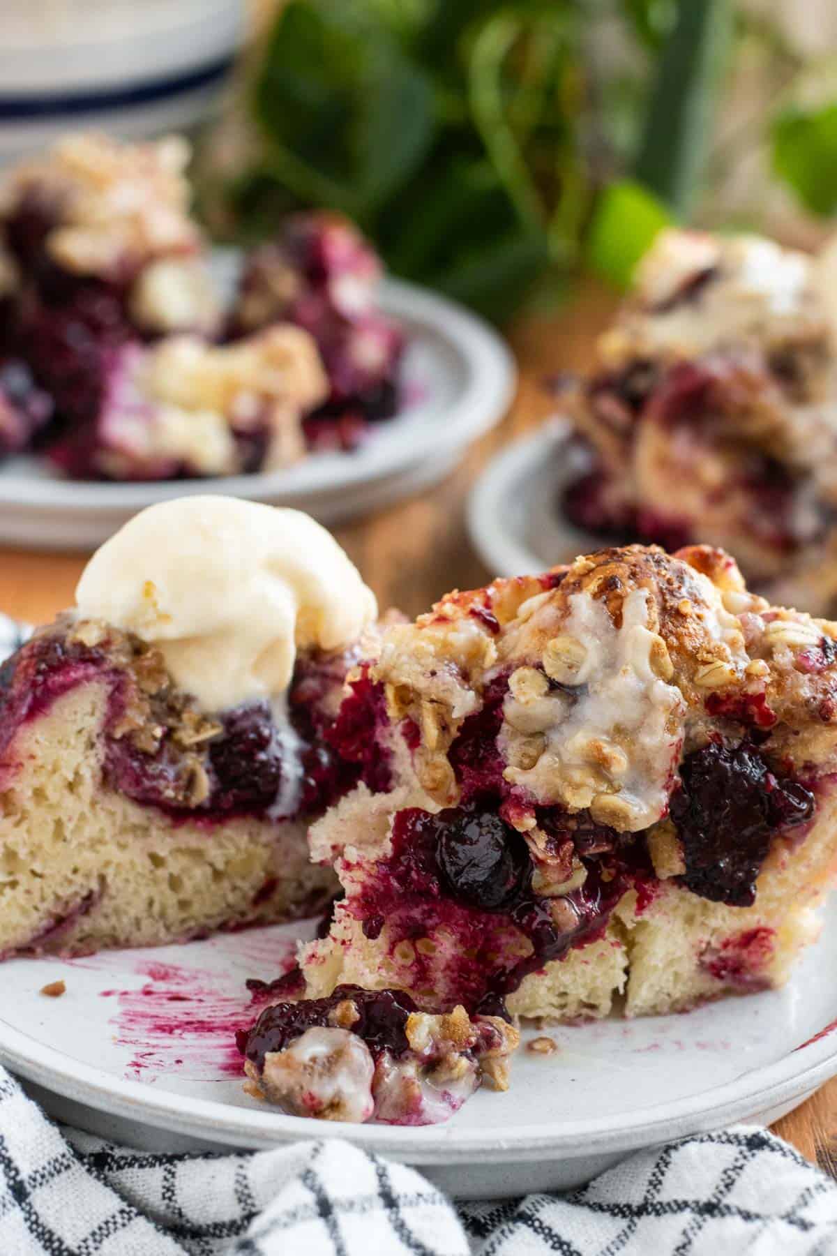 A large piece of berry focaccia cut in half on a plate to show the open crumb and blueberry filling inside.