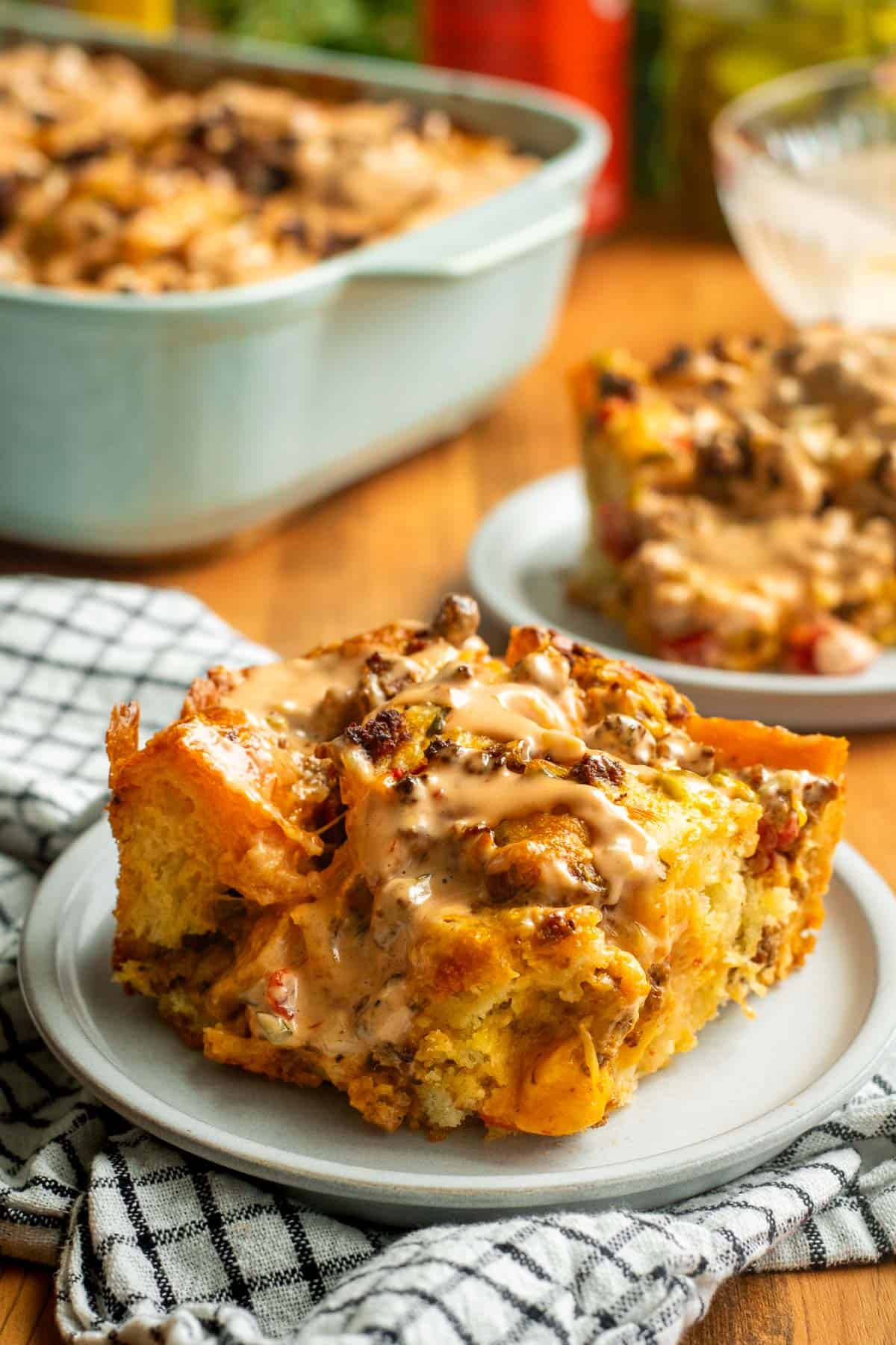 A large square of focaccia on a grey plate topped with ground beef, melted cheese, tomatoes, and light orange sauce.