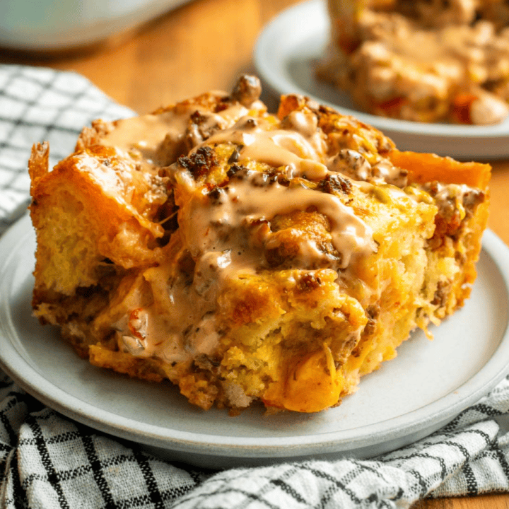 A large square of focaccia on a plate topped with browned ground beef, melted cheese, tomatoes, and burger sauce.