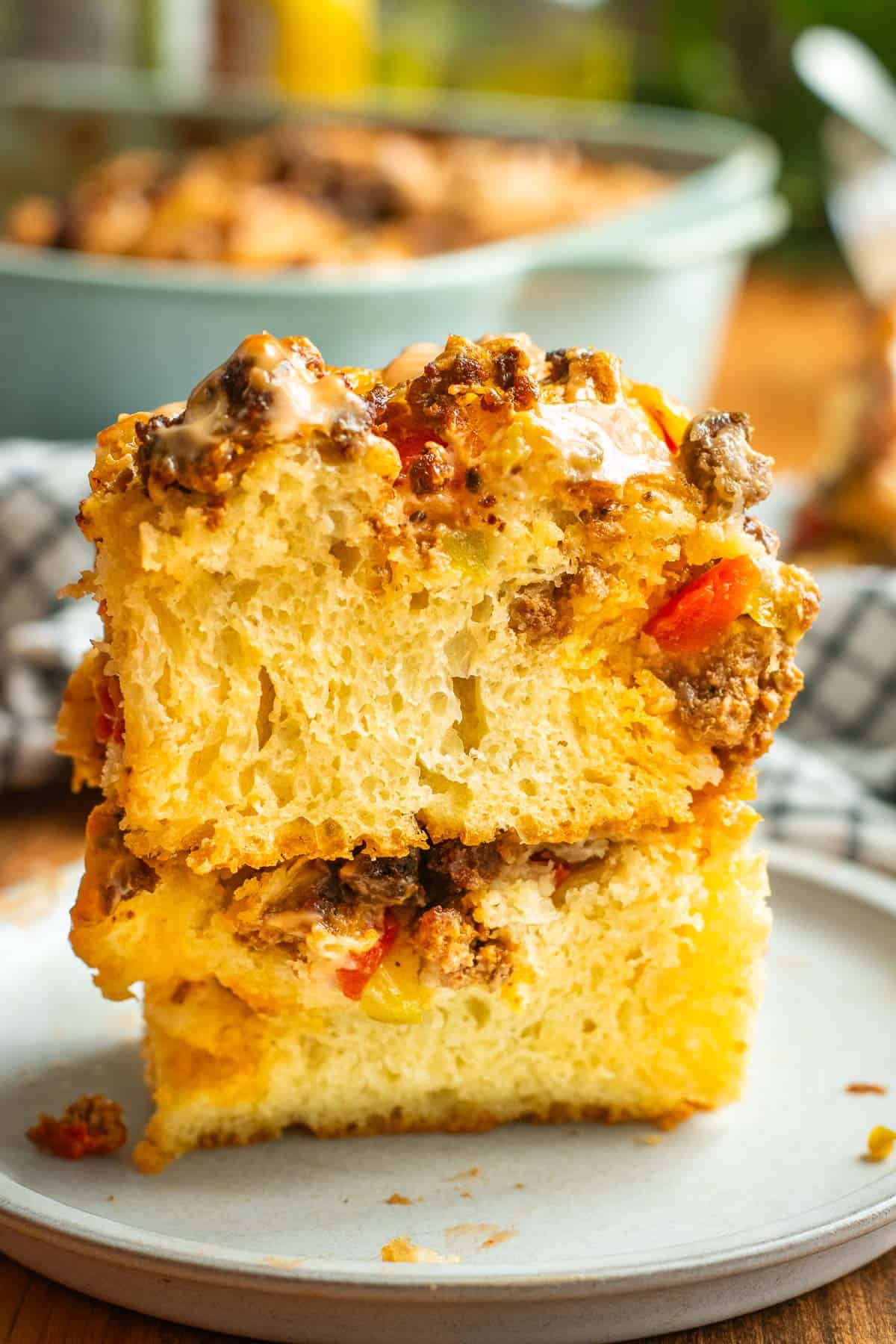 Two large, fluffy pieces of focaccia stacked on top of each other on a plate, topped with ground beef, melted cheese, tomatoes, diced pickles, and burger sauce.