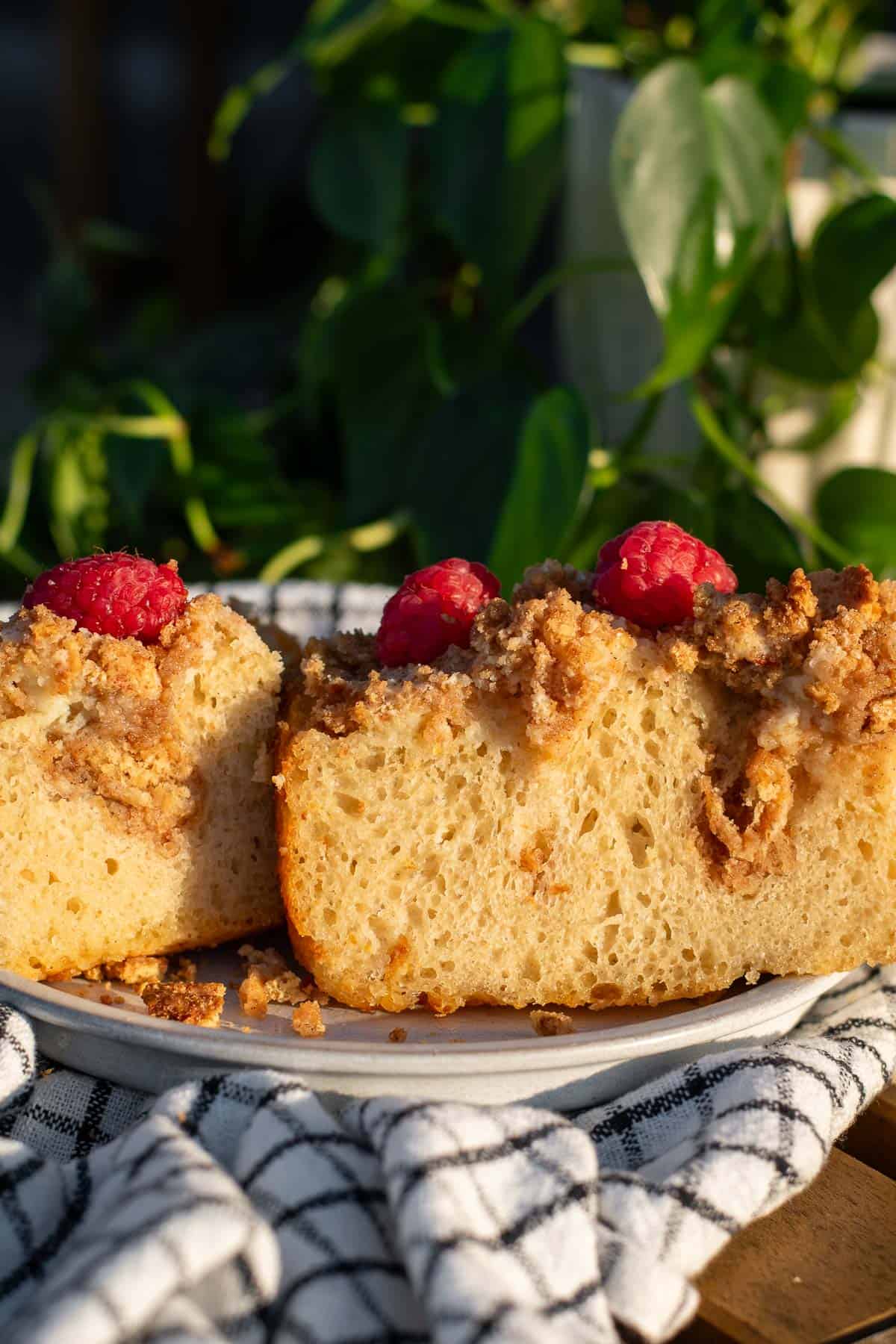 Two halves of a sweet focaccia bread topped and filled with cheesecake filling and crushed graham crackers, with fresh raspberries sitting on top.