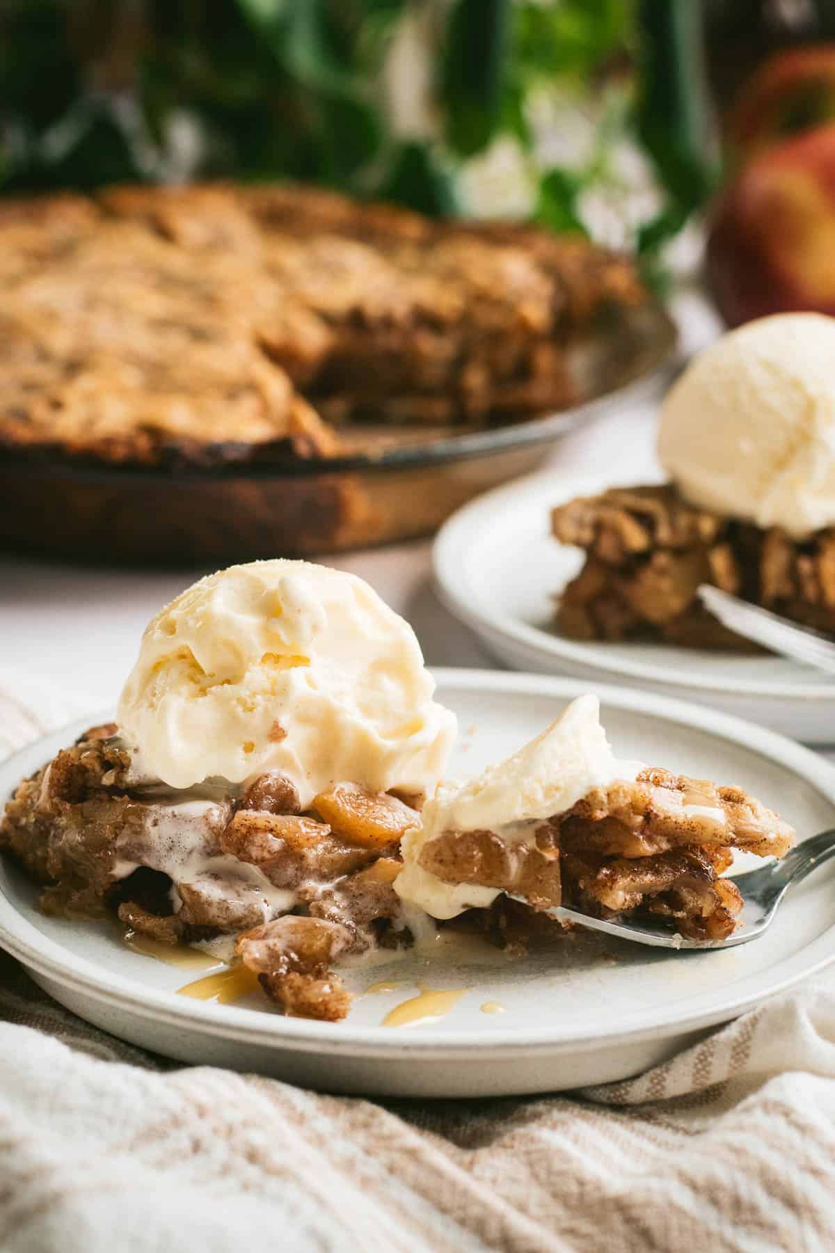 A half-eaten slice of apple pie topped with vanilla ice cream on a grey plate with a fork.