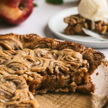 An apple pie in a glass dish topped with a cinnamon roll pie crust.