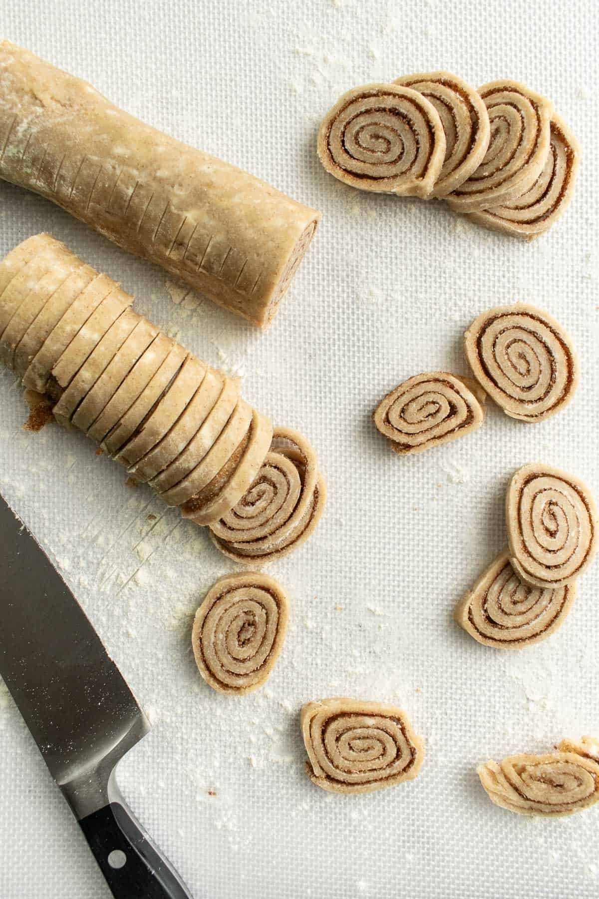 Small cinnamon-filled spirals of pie crust on a light surface next to a kitchen knife.