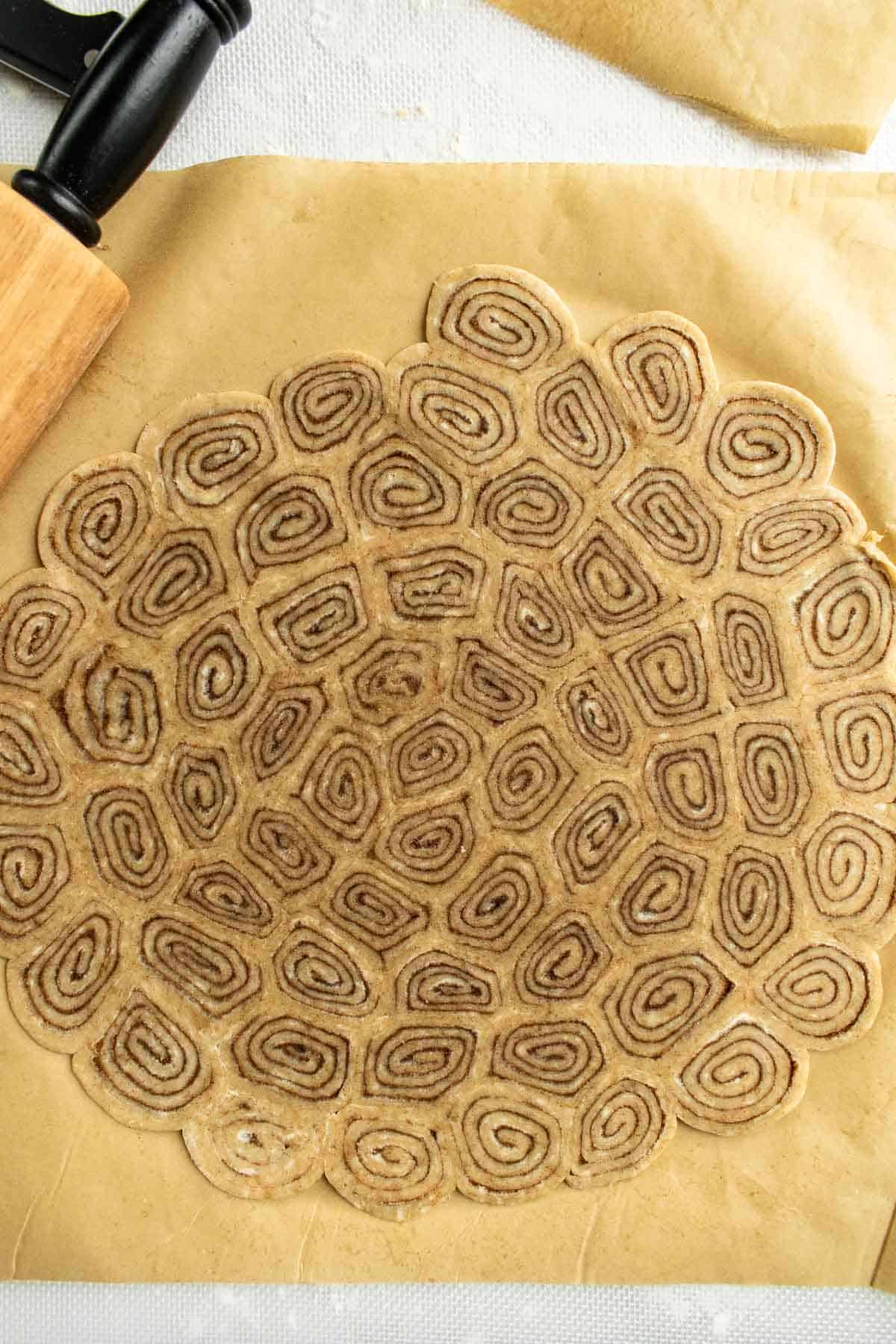 Mini cinnamon rolls made from pie crust pressed into a flat circle on parchment paper.