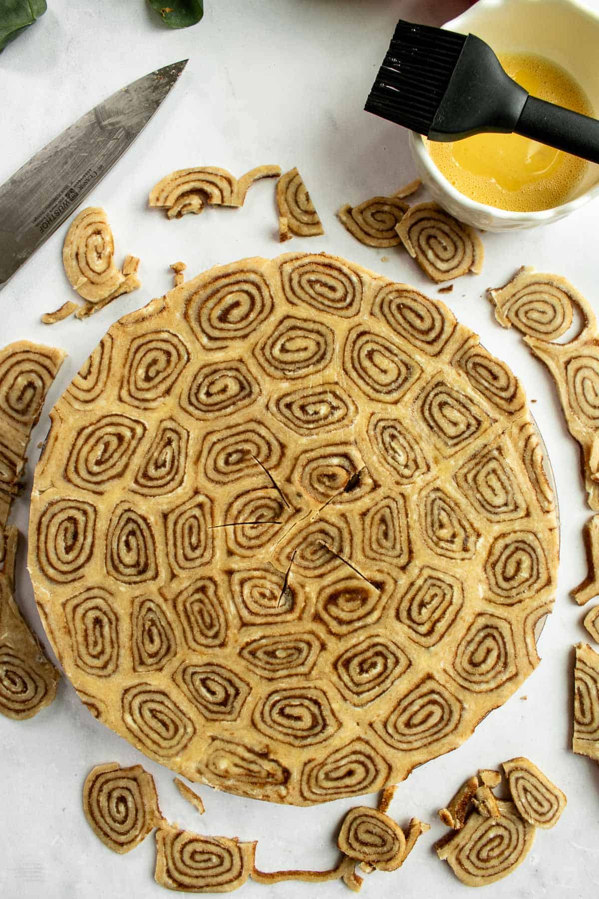 An unbaked cinnamon roll pie with the edges trimmed off on a light surface.