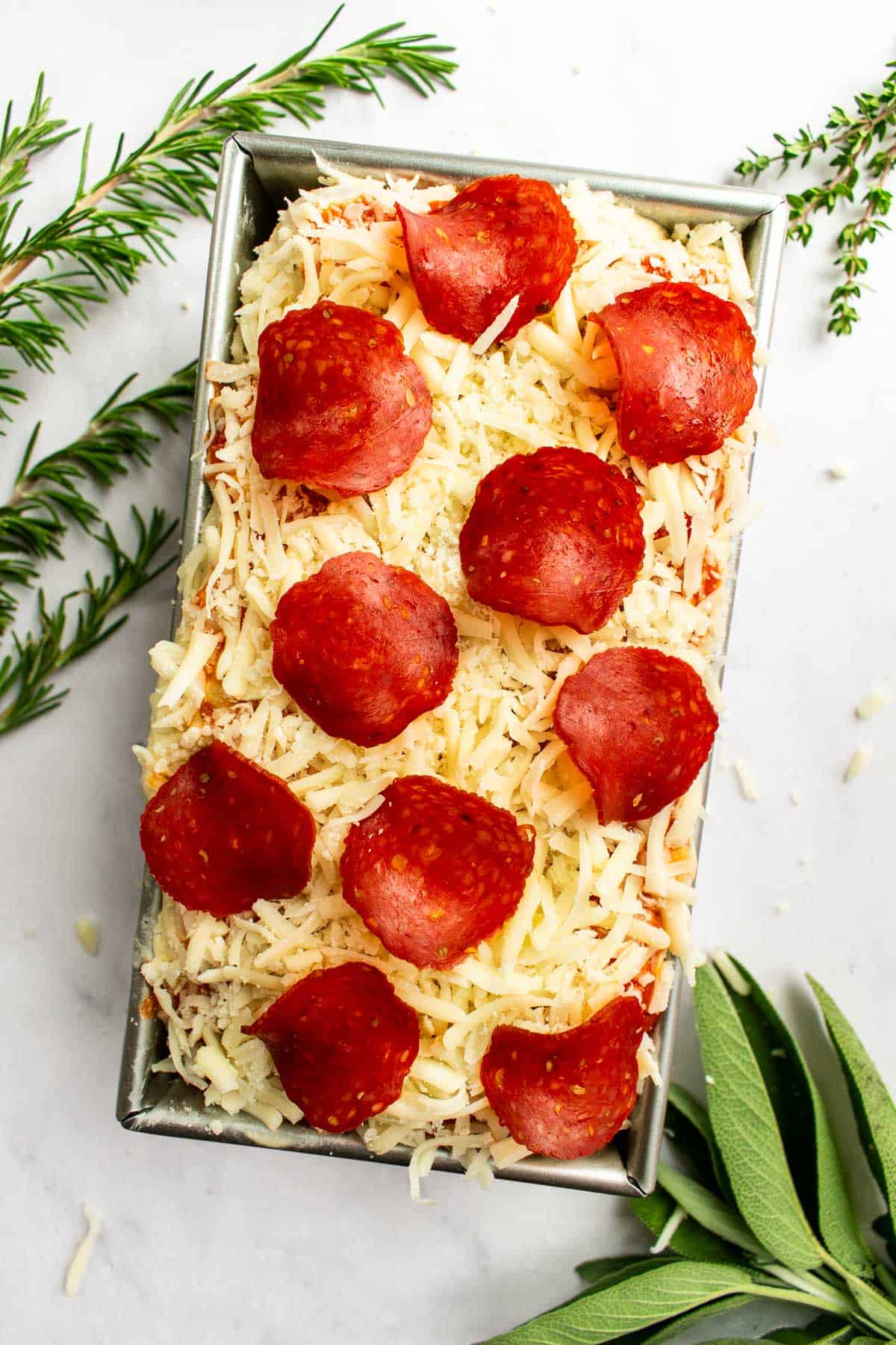 Risen, bubbly focaccia dough in a loaf pan topped with shredded cheese and pepperoni slices.