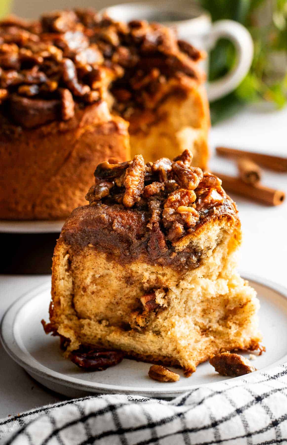 A fluffy cinnamon roll on a grey plate topped with caramelized brown sugar and pecans.
