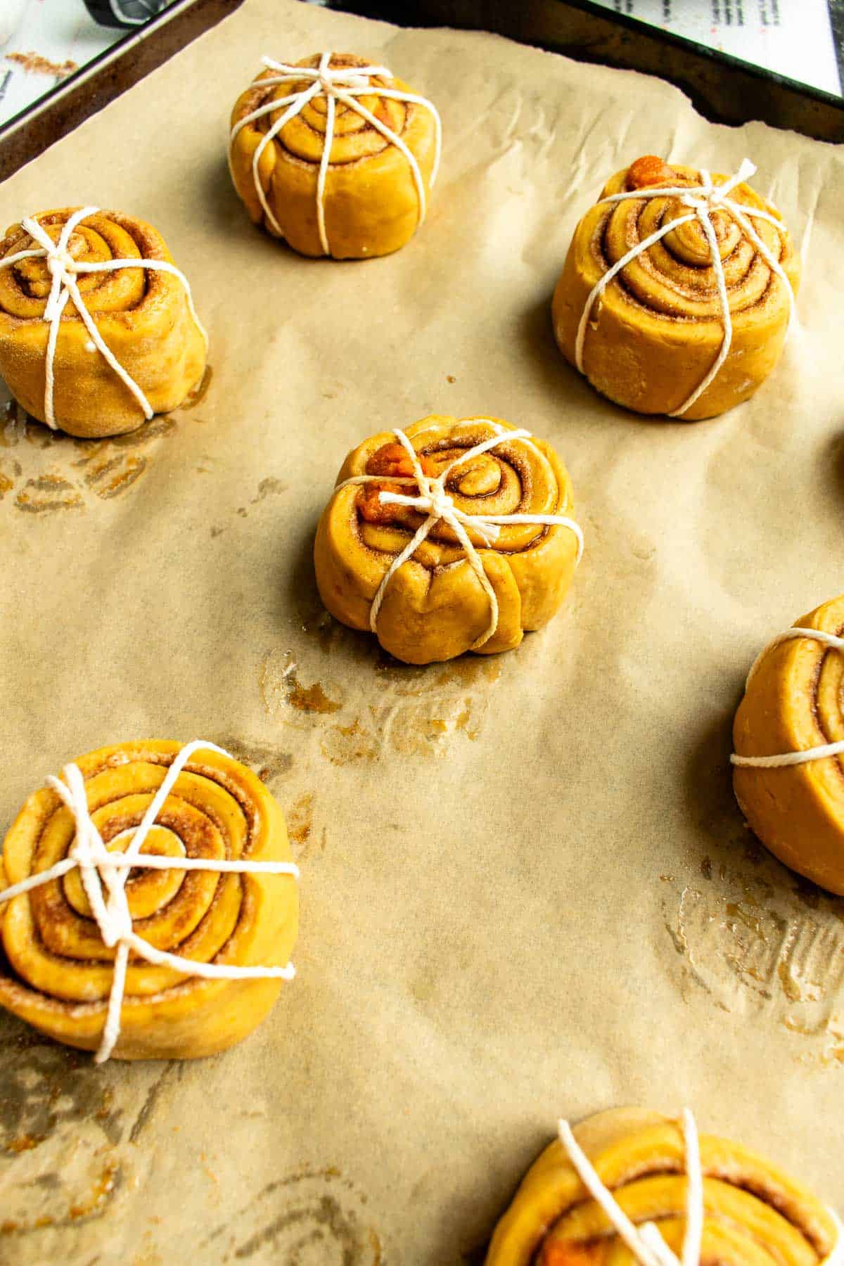 Cinnamon rolls wrapped in baking string on a baking sheet lined with parchment paper.