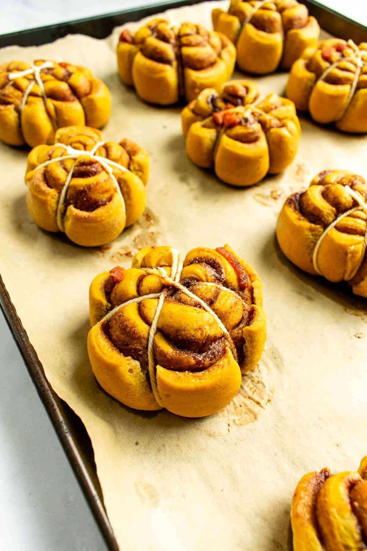 Pumpkin-shaped cinnamon rolls on a baking sheet wrapped in baking string.