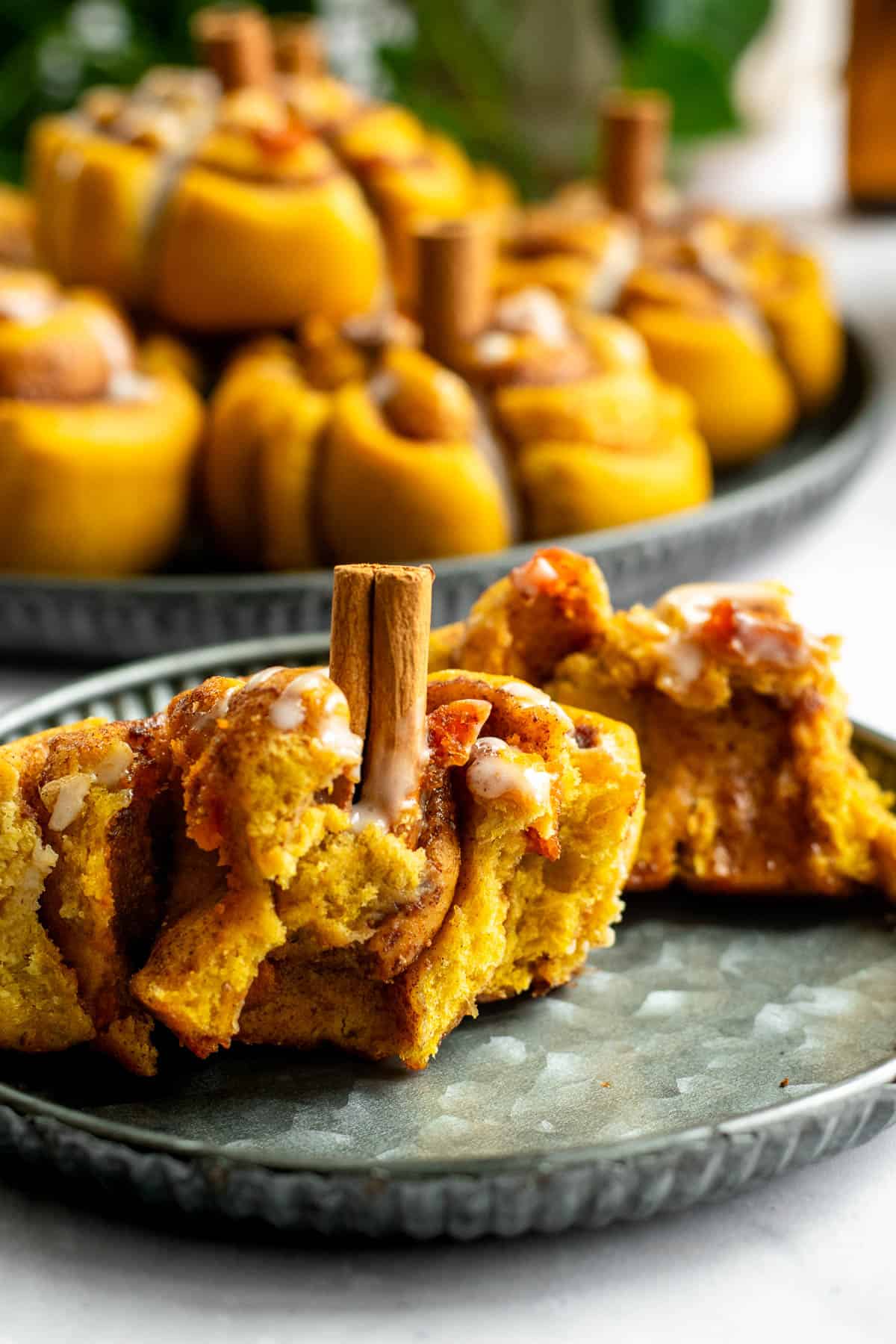 An orange pumpkin-shaped cinnamon roll torn in half to show the cinnamon swirl and fluffy crumb inside, sitting on a metal plate.