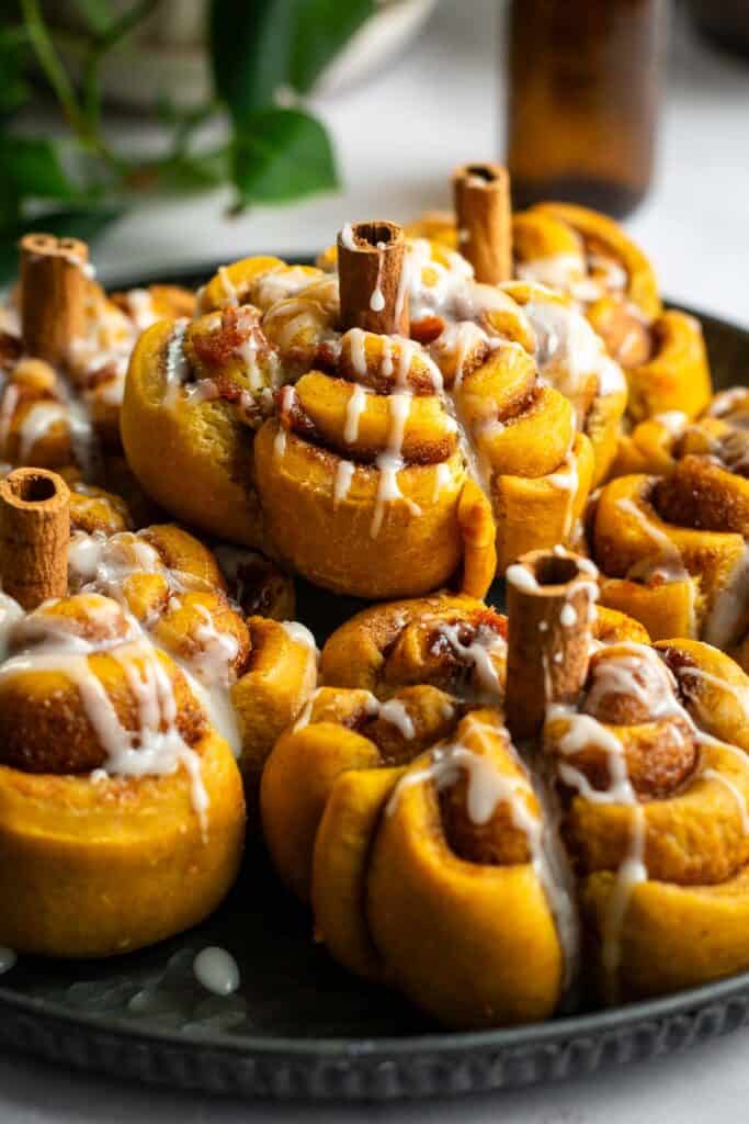 A metal plate topped with half a dozen glazed pumpkin-shaped cinnamon rolls with cinnamon stick stems.