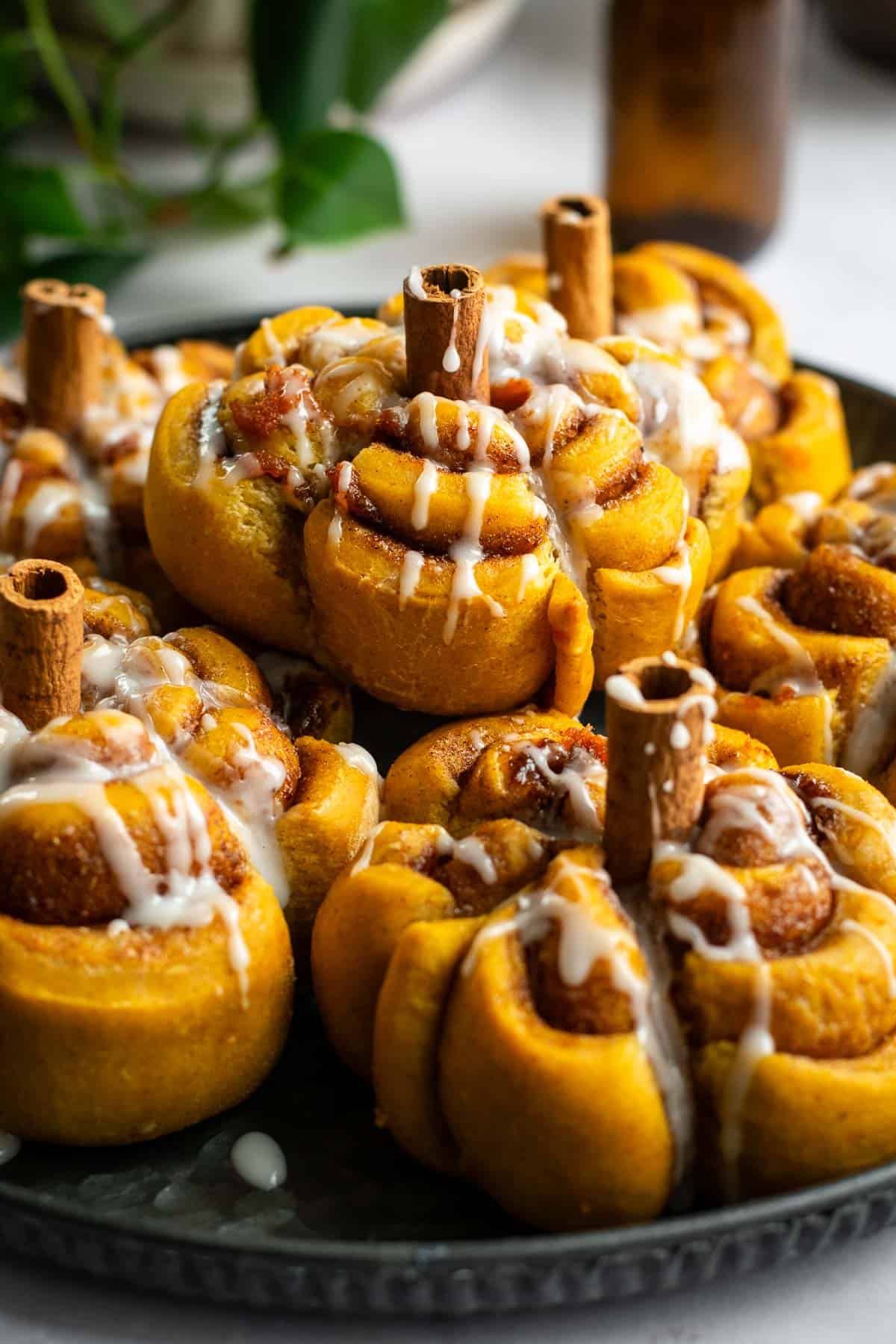 A metal plate topped with half a dozen glazed pumpkin-shaped cinnamon rolls with cinnamon stick stems.