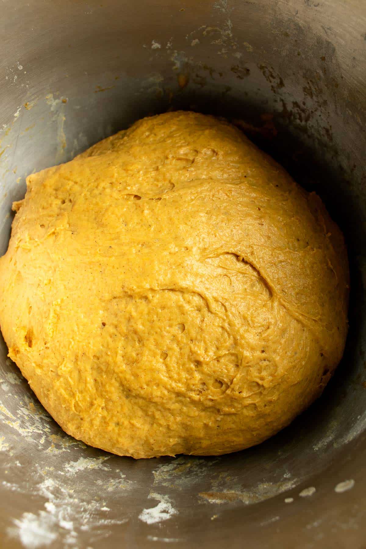 Orange pumpkin yeast dough in a metal mixing bowl.
