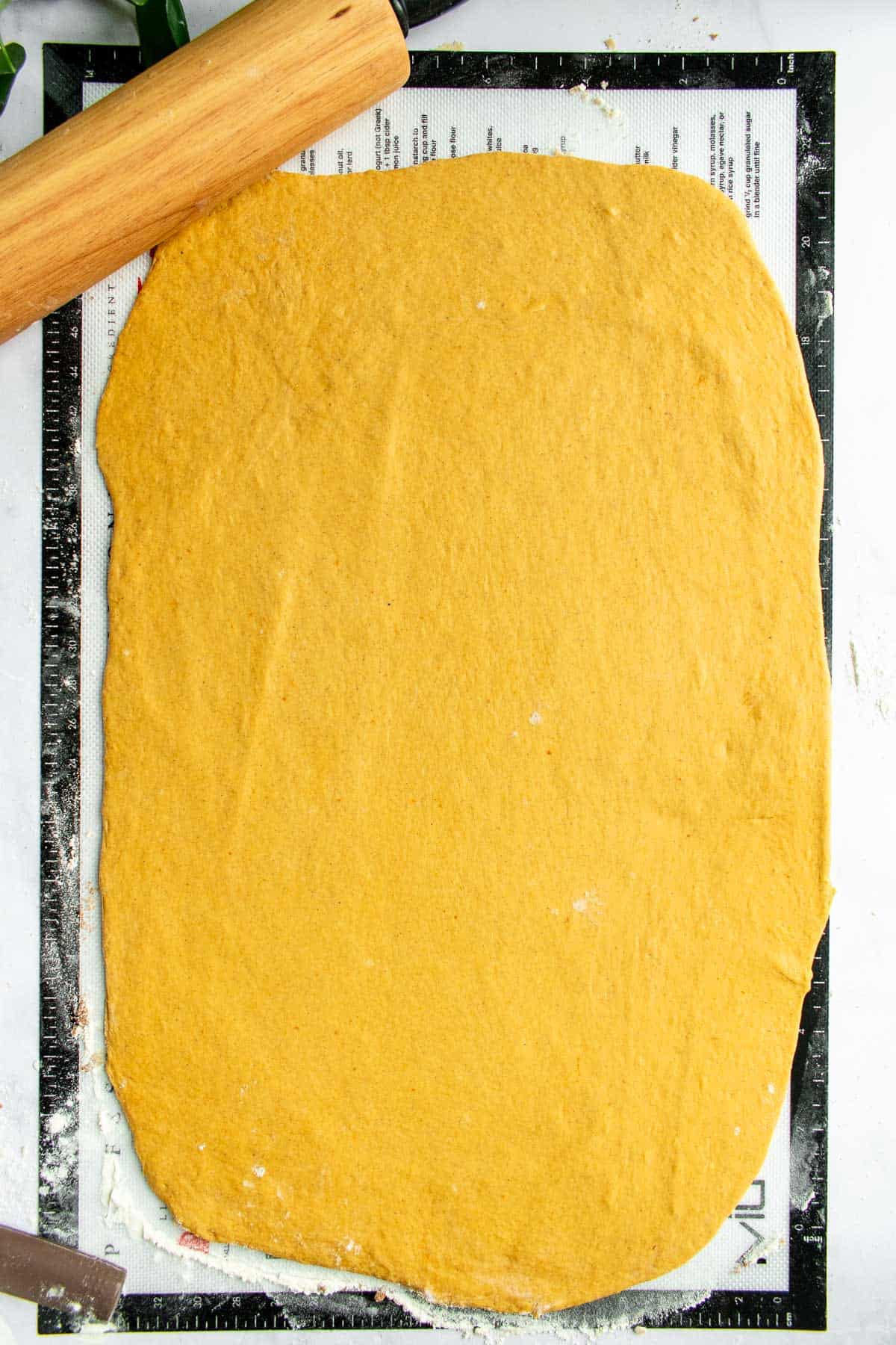 Pumpkin bread dough rolled out in a large rectangle next to a rolling pin.