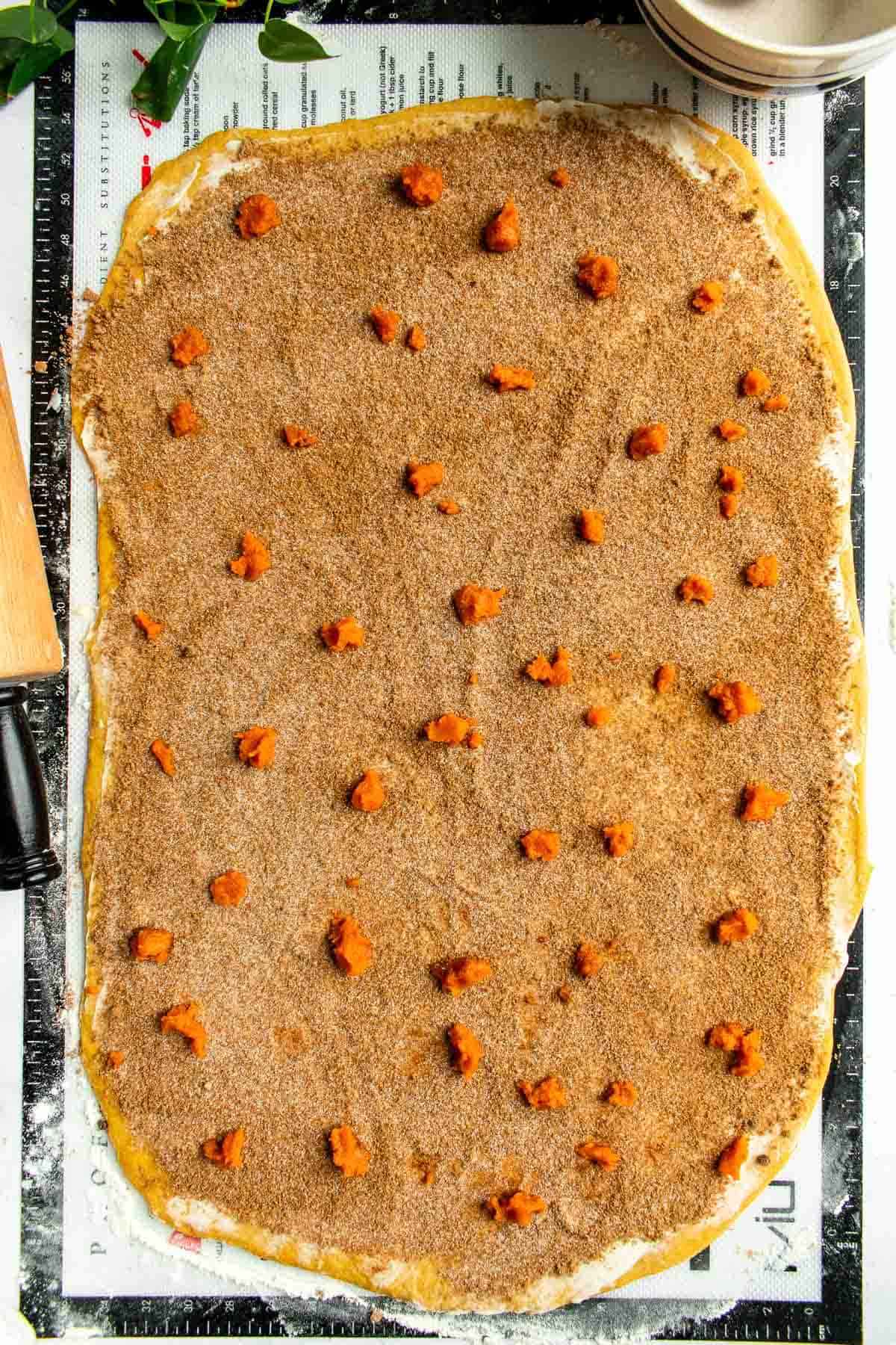 Rolled-out cinnamon roll dough topped with butter, cinnamon sugar, and small dollops of pumpkin puree.
