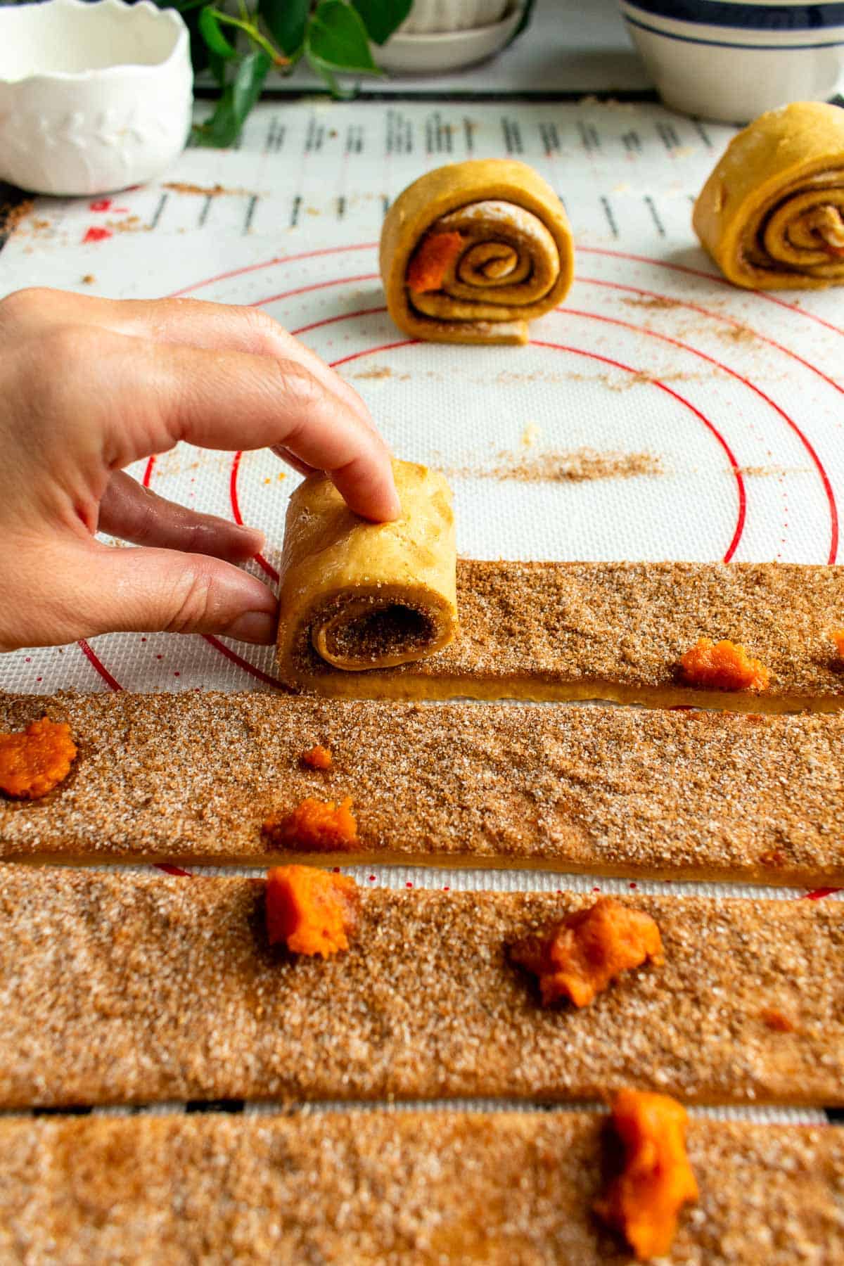 A hand rolling a strip of cinnamon-sugar-coated dough into a spiral.