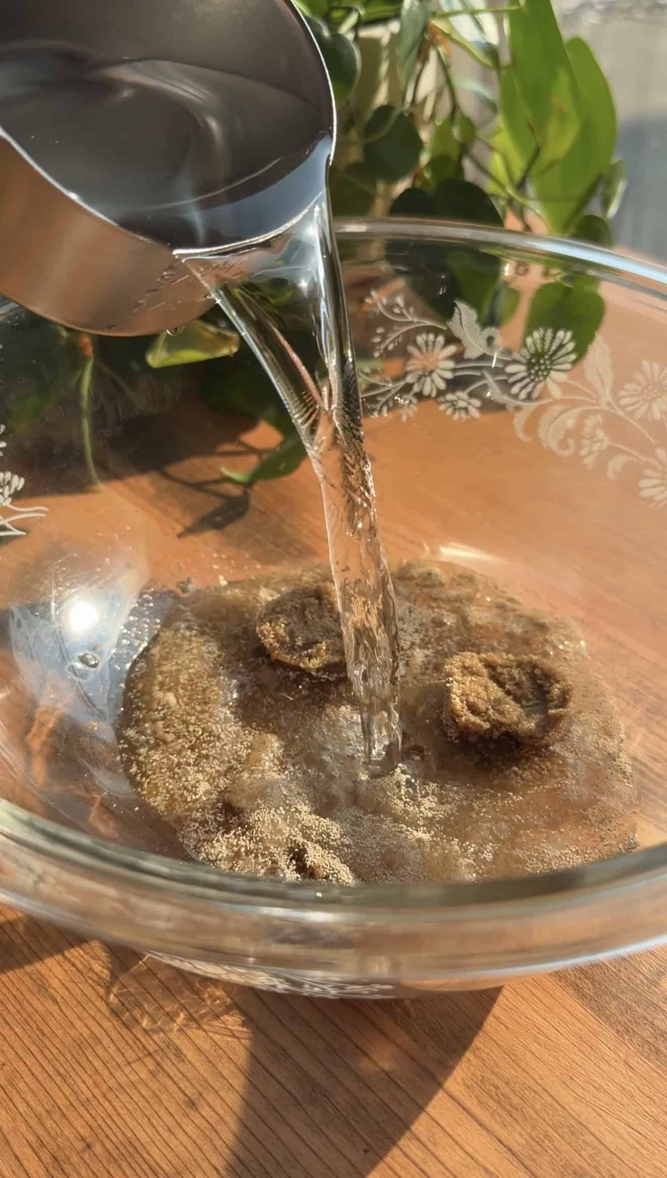 Water pouring from a measuring cup into a bowl with brown sugar and dry yeast in it.