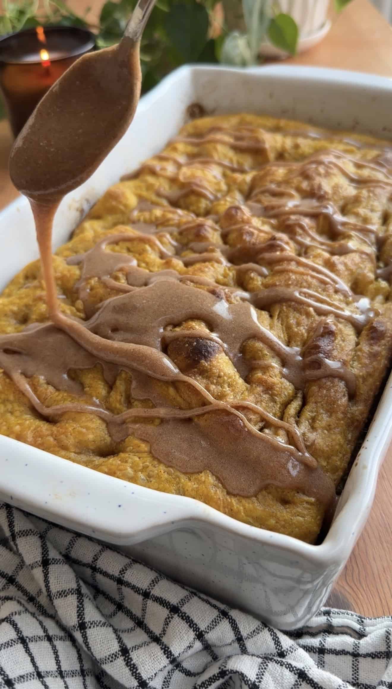Light brown glaze bring drizzled onto baked, golden focaccia in a white baking dish.